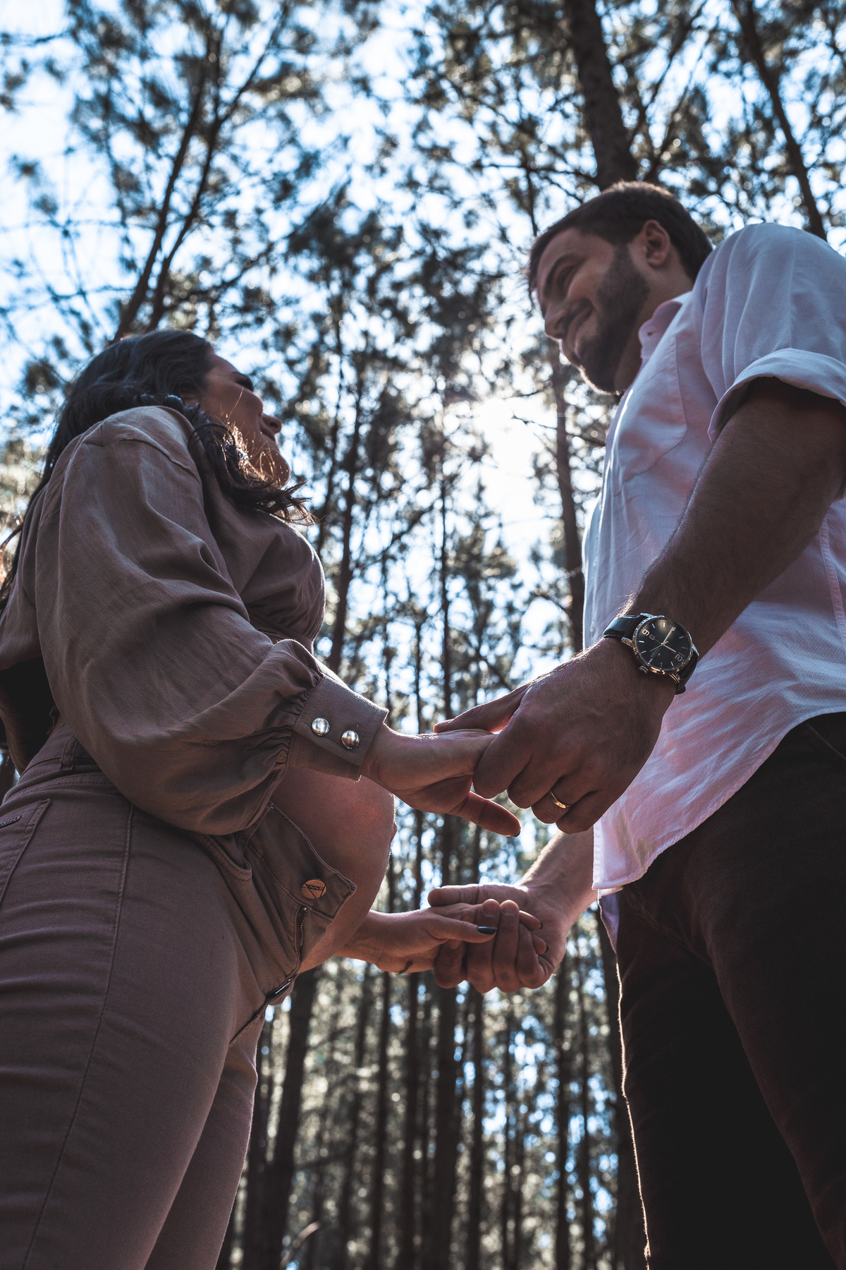 casal grávidos de mãos dadas se olhando em parque com árvores em Florianópolis