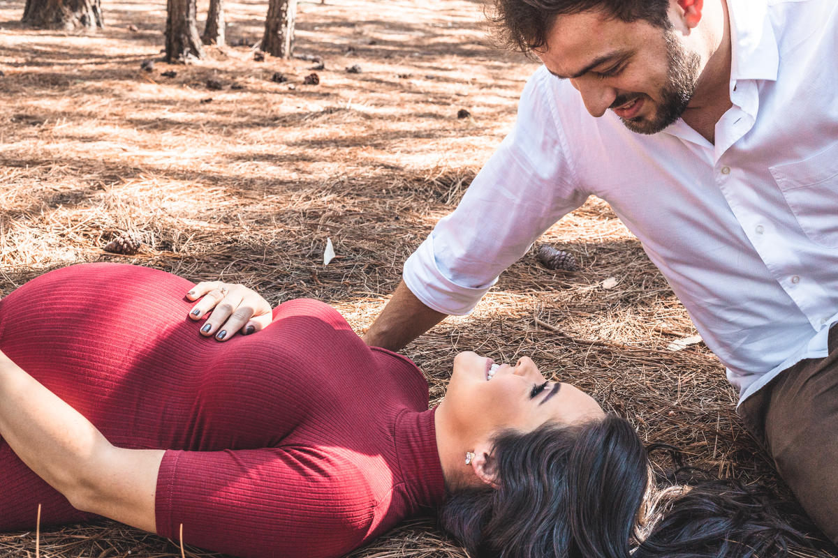 gestante deitada em chão de parque olhando para o marido que está sentado admirando-a