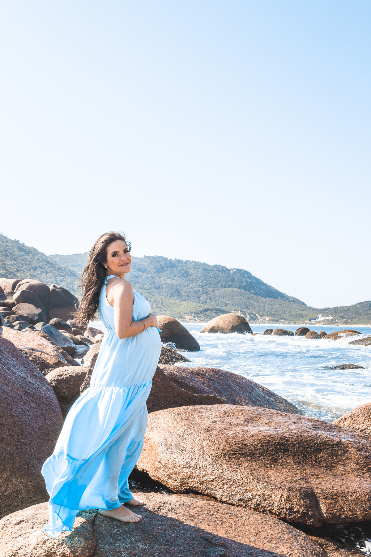 gestante de vestido azul nas pedras da praia de Florianópolis