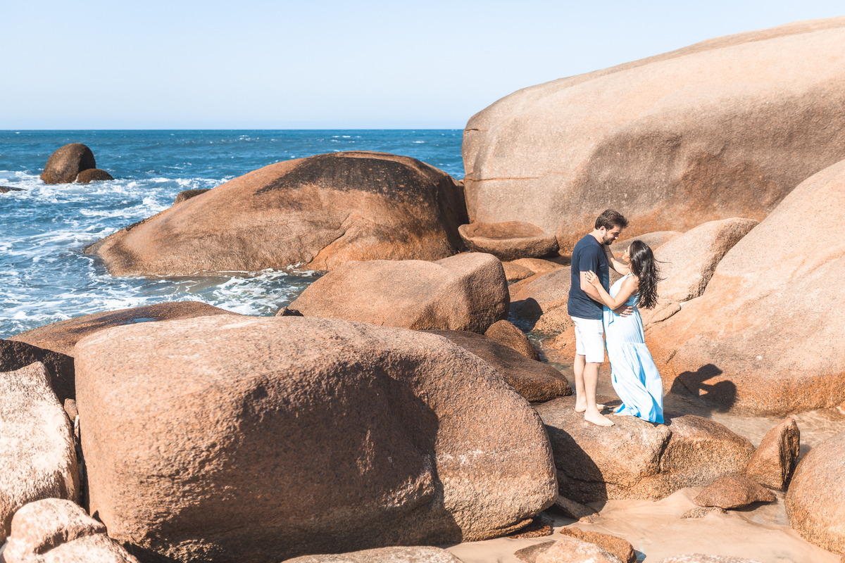 casal grávidos de roupa azul nas pedras da praia de Florianópolis
