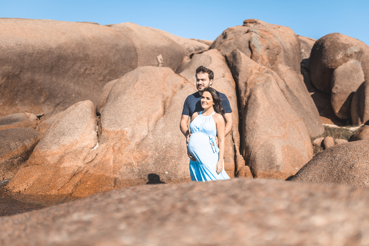 casal grávidos de roupa azul na praia olhando para o horizonte