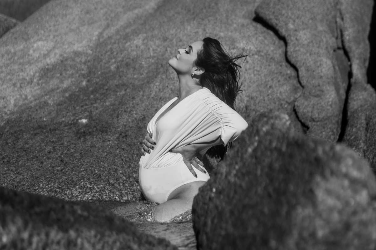 gestante de body ajoelhada na água e de olhos fechados. foto em preto e branco 