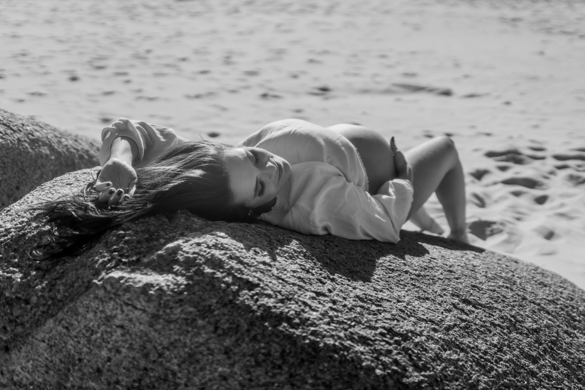 gestante de top deitada na pedra na praia mostrando a barriga