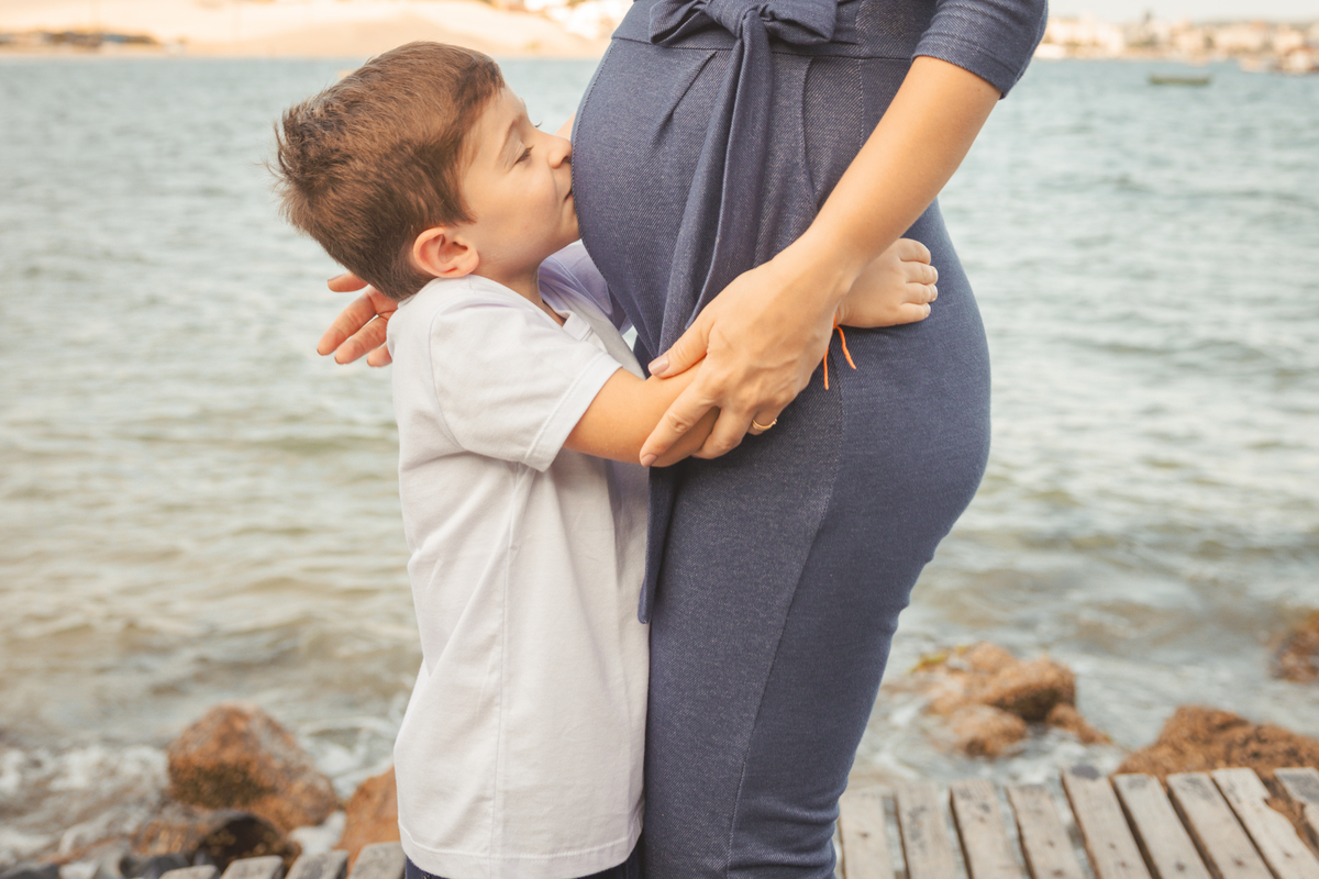 filho beijando a barriga da mãe grávida na praia de Florianópolis
