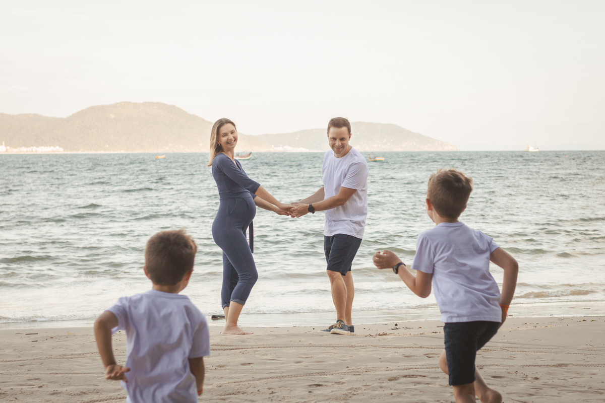 filhos correndo em direção aos pais na praia. mulher gestante