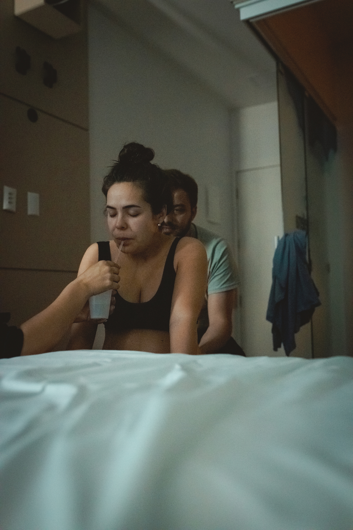 gestante sentada na bola, tomando água, com o marido atrás dando suporte, em sala de parto