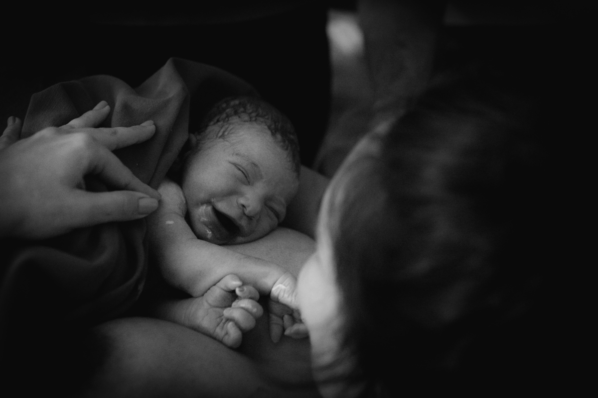 foto em preto e branco de bebê no colo da mãe, sorrindo, logo após o nascimento.