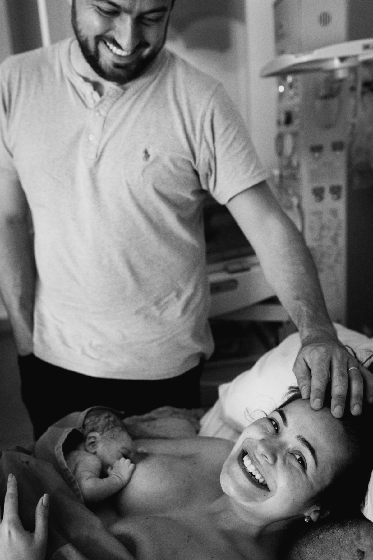 foto em preto e branco de pai fazendo carinho na mãe com bebê no colo, logo após o nascimento