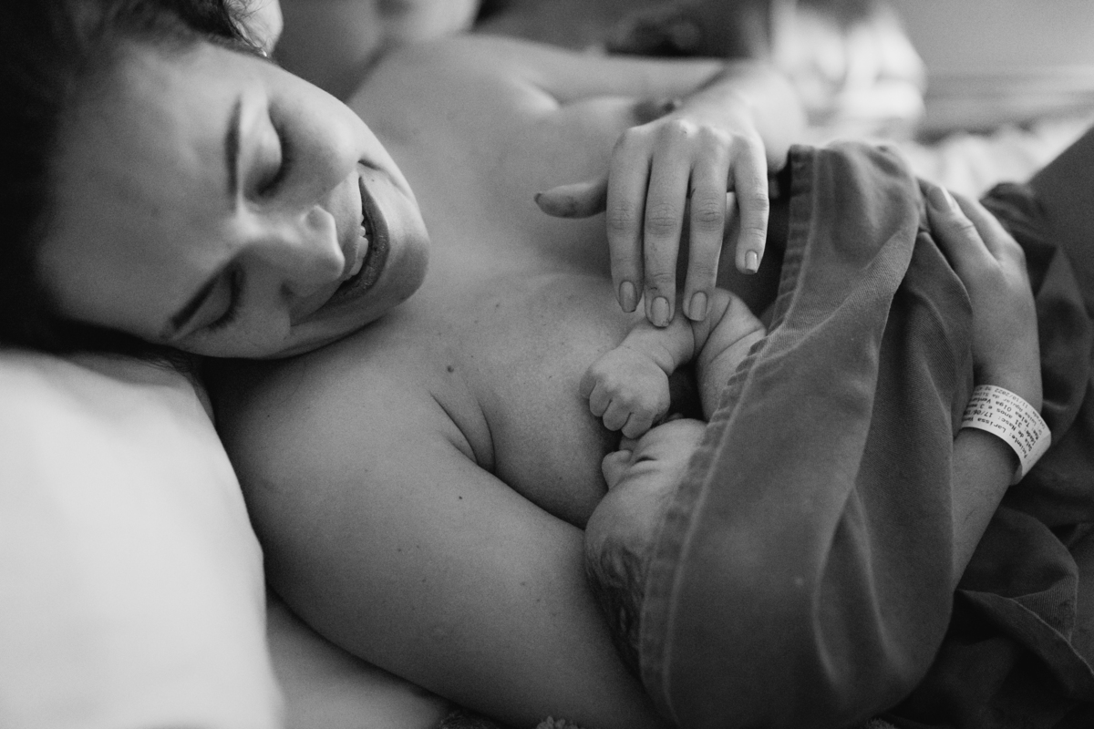 foto em preto e branco de mãe admirando seu bebê recém nascido em seu colo.