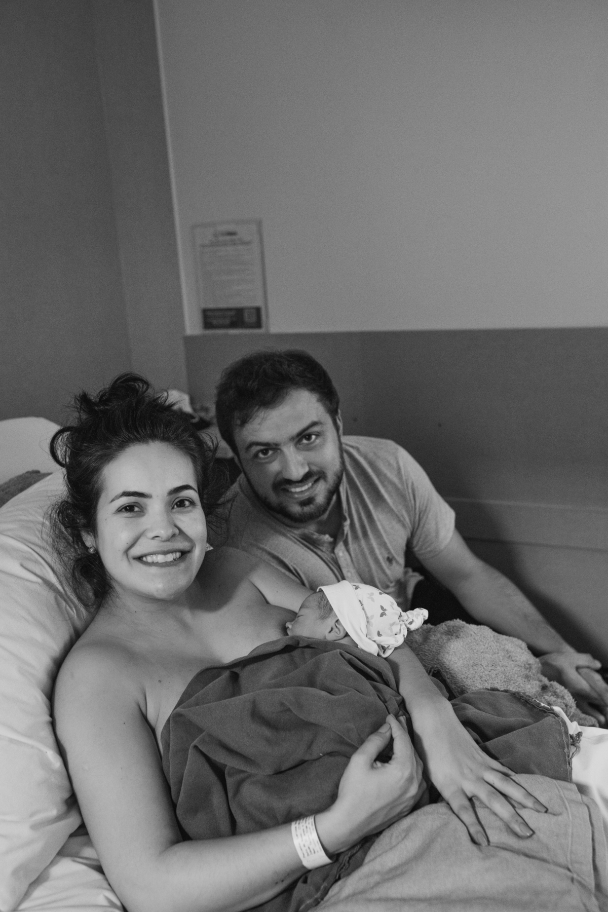 foto em preto e branco de bebê sendo amamentado enquanto pais sorriem para a foto