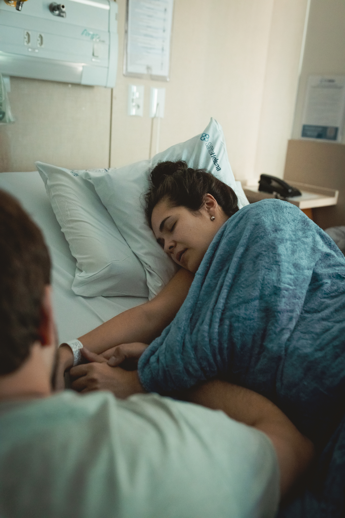 gestante em trabalho de parto, deitada na cama e segurando a mão do marido
