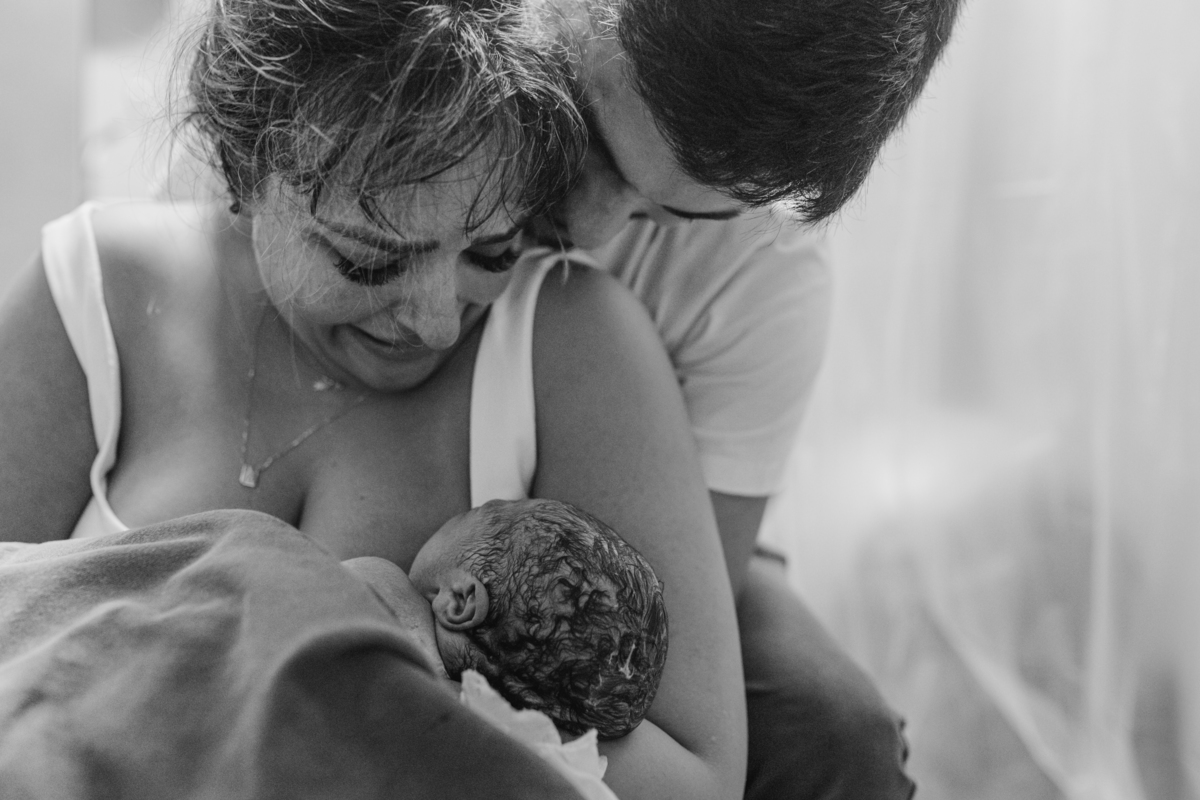 foto em preto e branco de pais emocionados carregando o bebê logo após o nascimento.