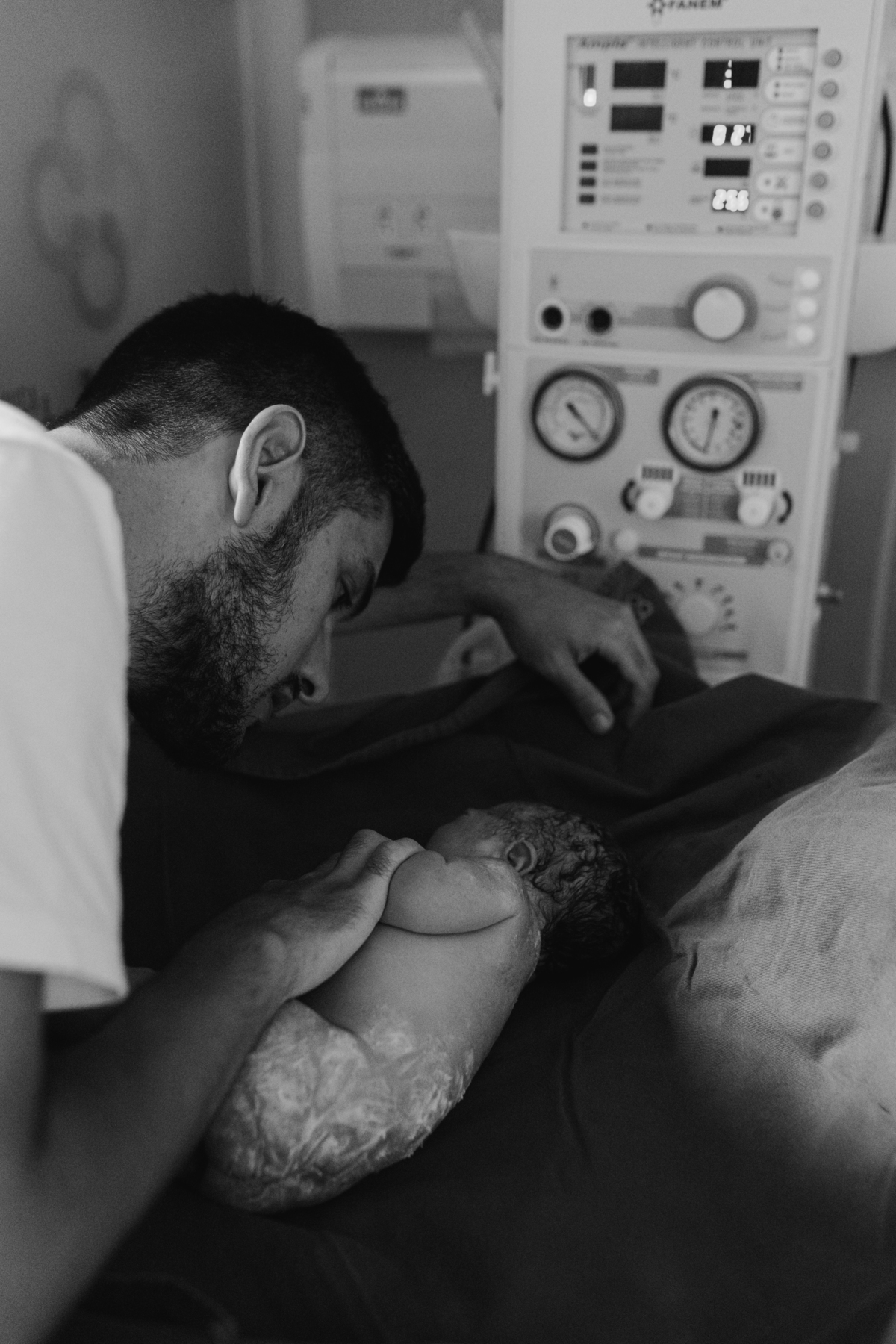 foto em preto e branco de pai conversando com o bebê que está no berço aquecido