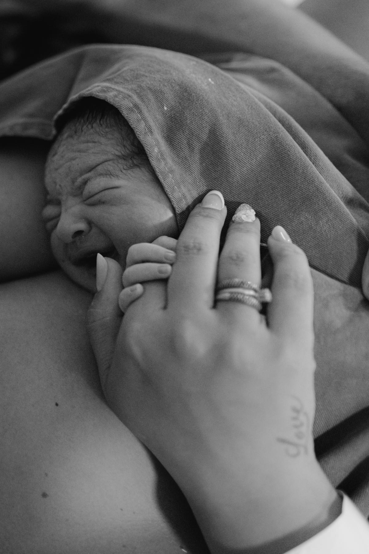 foto em preto e branco de bebê chorando e segurando na mão da mãe logo após o nascimento