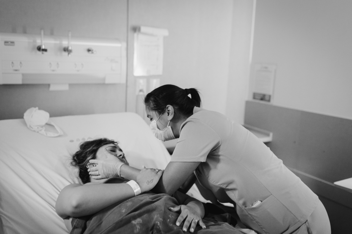 foto em preto e branco de doula parabenizando pelo parto a gestante que está deitada na cama .