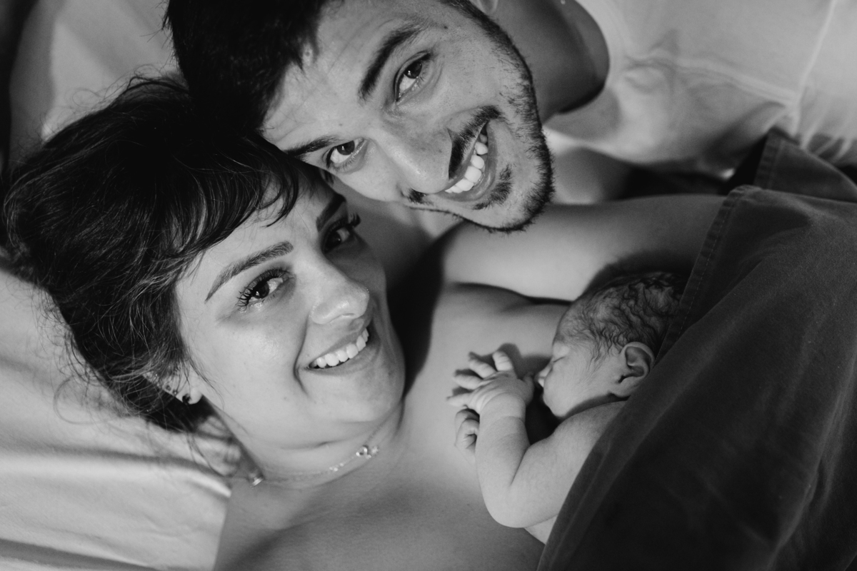 foto em preto e branco de pais com bebê no colo sorrindo para a câmera