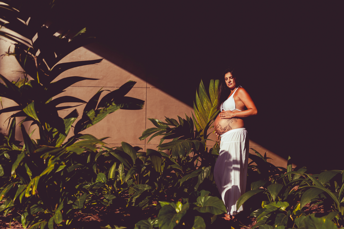 gestante de roupa branca no meio de um jardim com sol e sombra