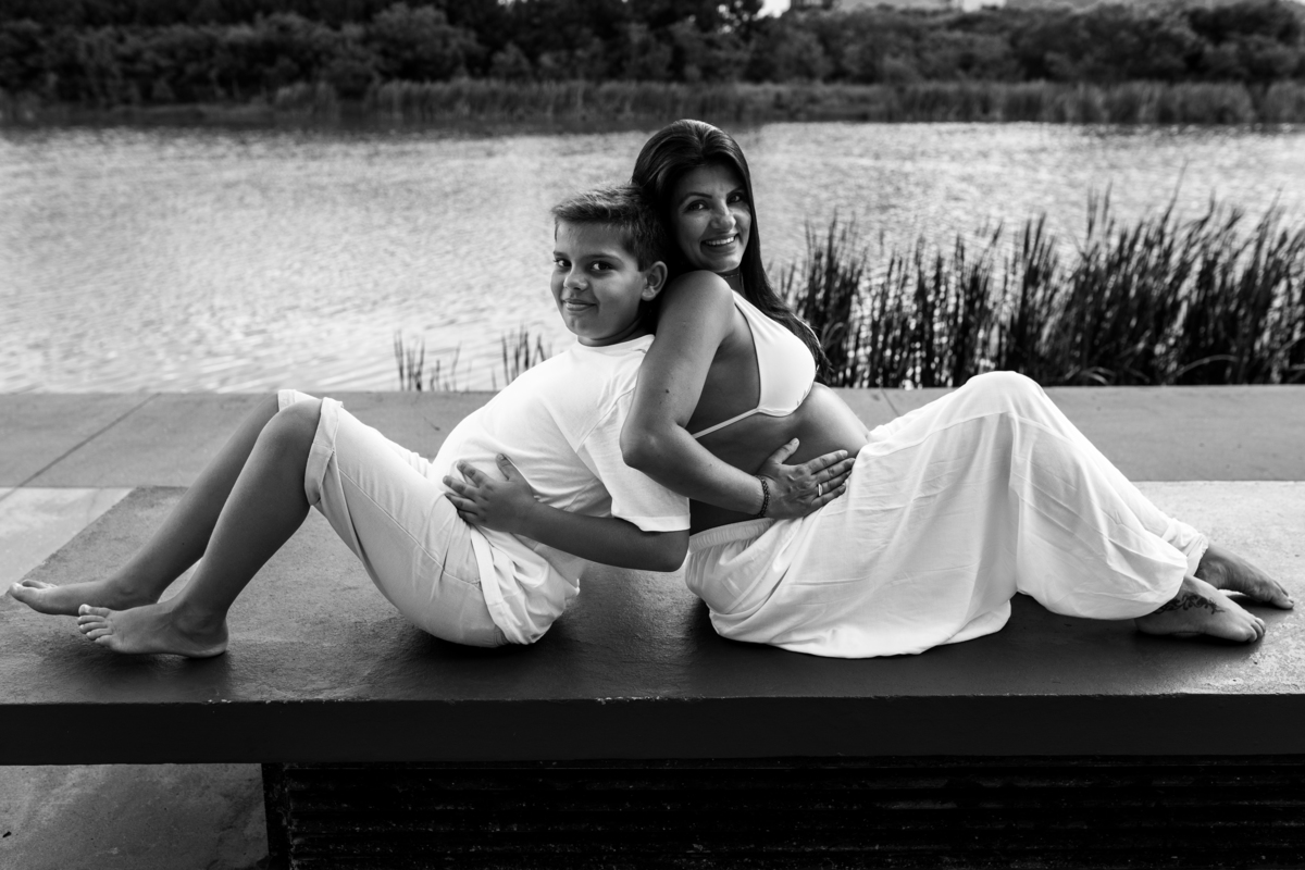 mae gestante e filho sentados em banco um de costas apoiado no outro mostrando a barriga