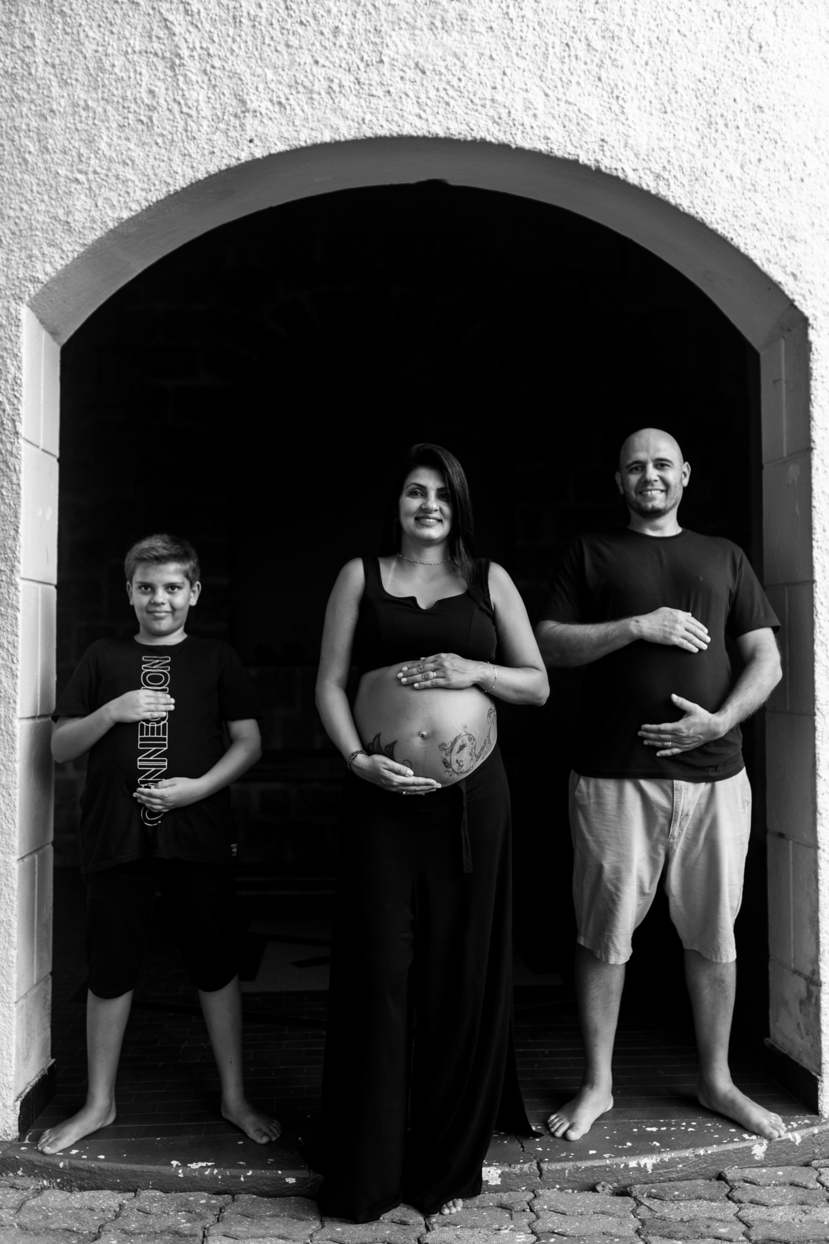 foto em preto e branco de gestante, marido e filho segurando a barriga em Florianópolis