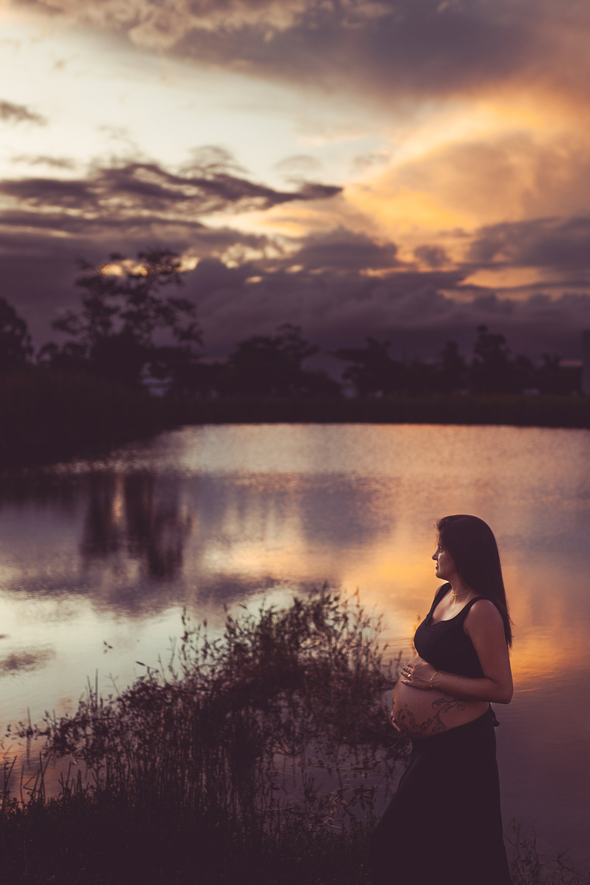foto de gestante em frente a um lago com reflexo do céu rosa no final da tarde