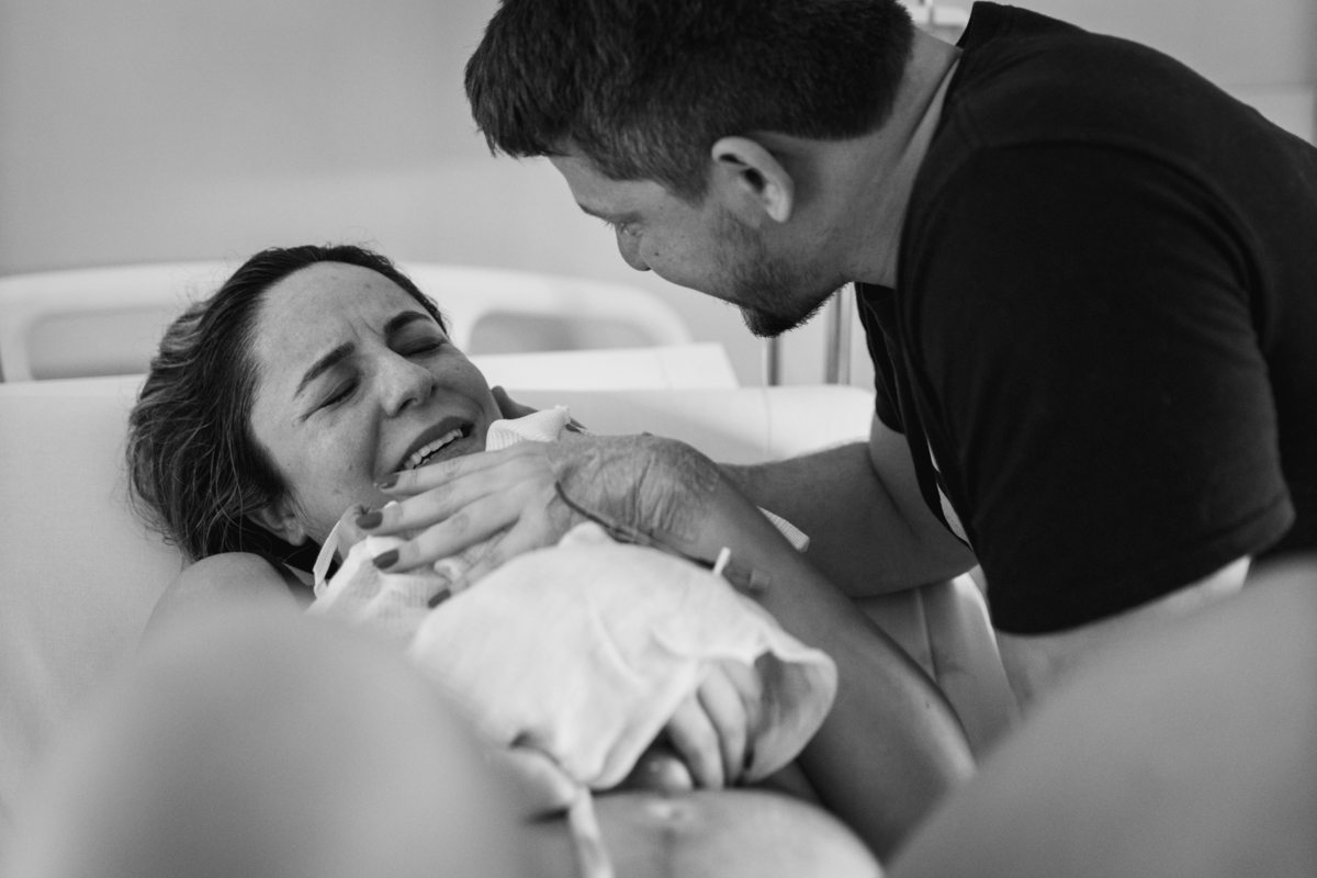 gestante emocionada que acabou de parir e pegar seu filho no colo, junto com o marido em preto e branco