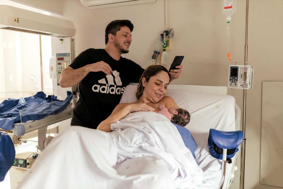 pai tirando foto do filho que acabou de nascer e está no colo da mãe