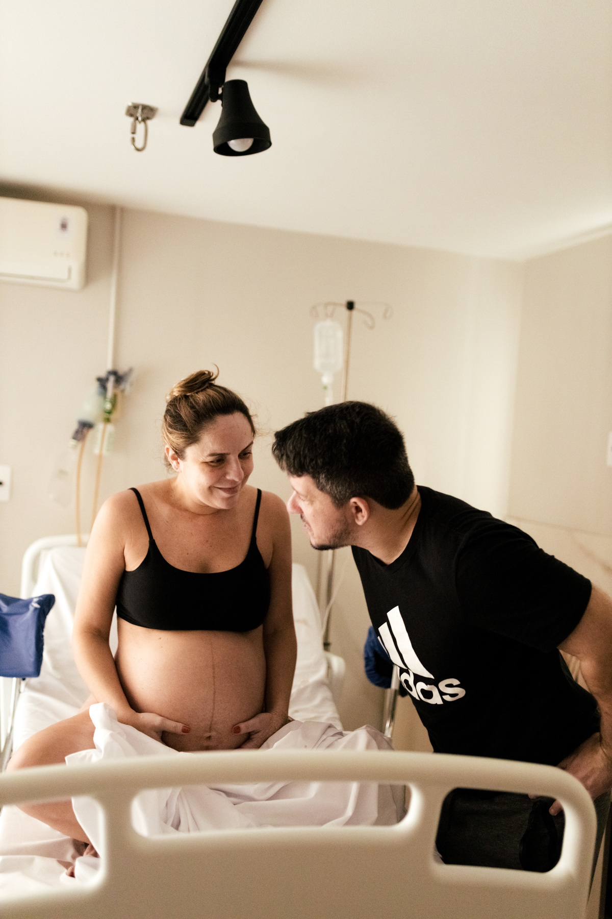 gestante em trabalho de parto sentada na cama da maternidade conversando com o marido