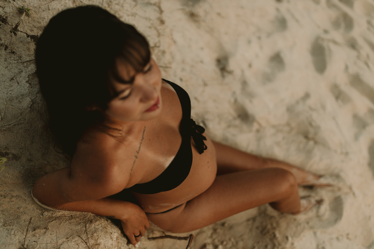 foto feita de cima de gestante de biquíni sentada na areia