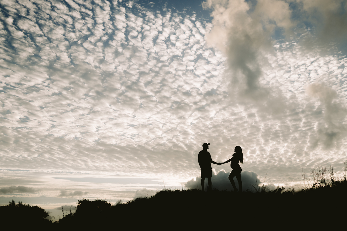foto em contra luz de casal grávidos em cima do morro