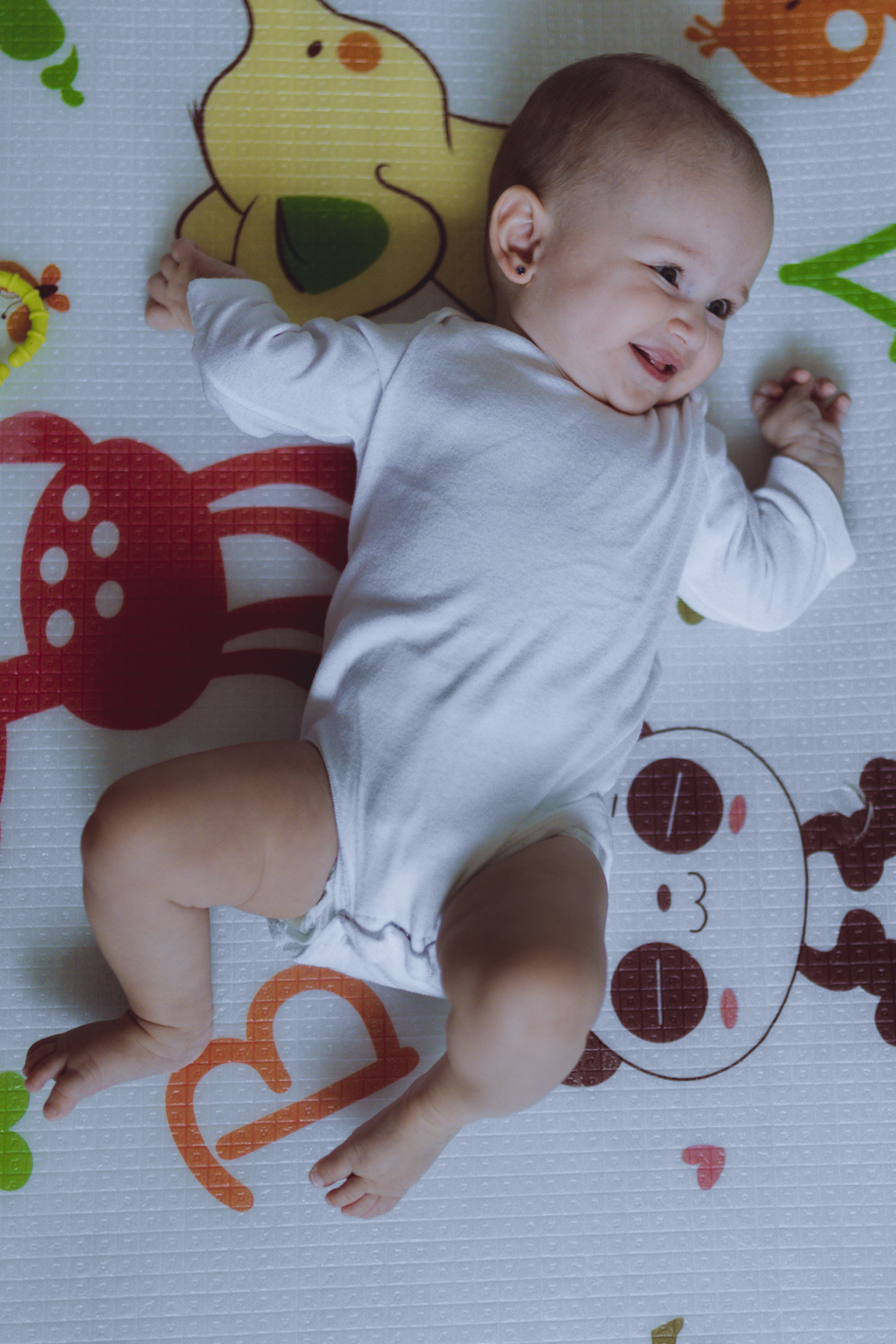 bebê sorrindo deitado no tapete de brinquedos 
