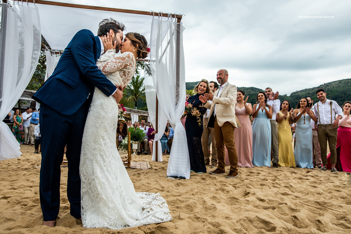 noivos se beijando com madrinhos ao lado em cerimônia ao ar livre casamento na praia em toque toque pequeno litoral de são paulo fotógrafo rafael bigarelli