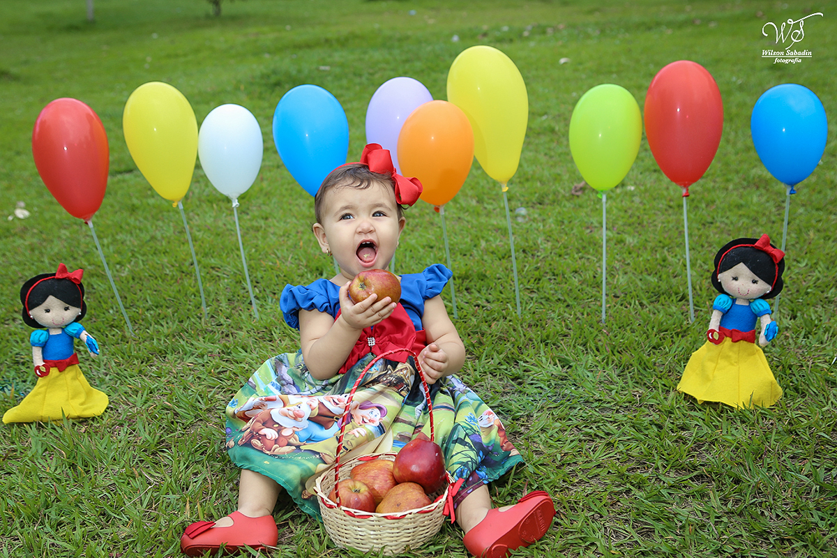 fotografia infantil sentada na grama comendo maçãs