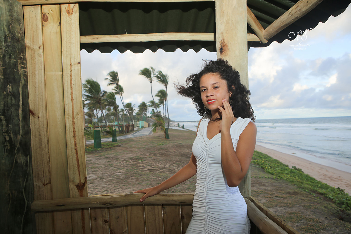 fotografia de 15 anos a debutante dentro da cabana de praia com a mão no rosto