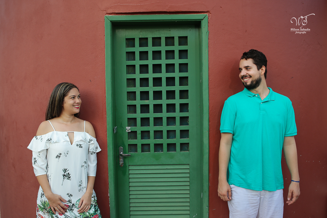 os noivos encostados na parede vermelha e ao meio uma porta verde