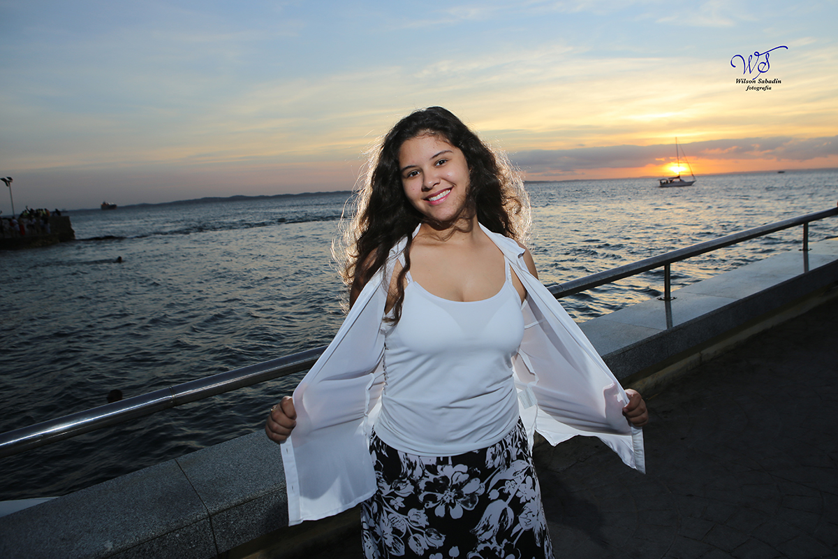 Ensaio de 15 anos, a debutante Vitória com pôr do sol e veleiro passando ao fundo