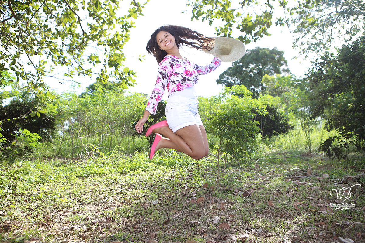 fotografia de 15 a debutante pulando no pomar da fazenda