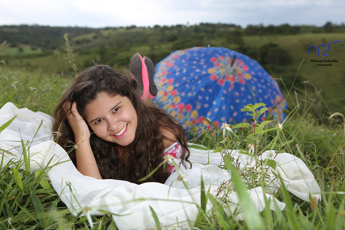fotografia de 15 a debutante deitada na grama e ao fundo um guarda chuva colorido