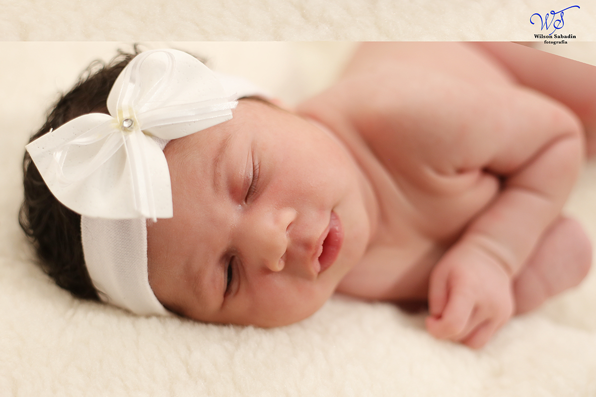 Fotografia de newborn em Salvador, o bebe dormindo com laço branco na cabeça