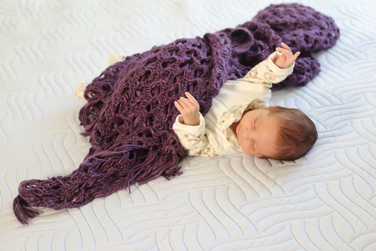 Fotografia de newborn em Salvador, o bebe mexendo as mãozinhas  e manta roxa