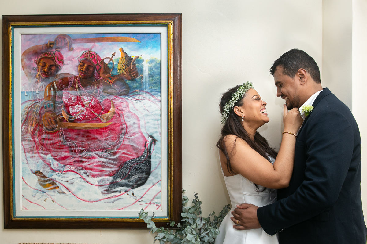 fotografia de casamento em Salvador Bahia, noivos abraçados ao lado da sua obra de arte em motivos religiosos