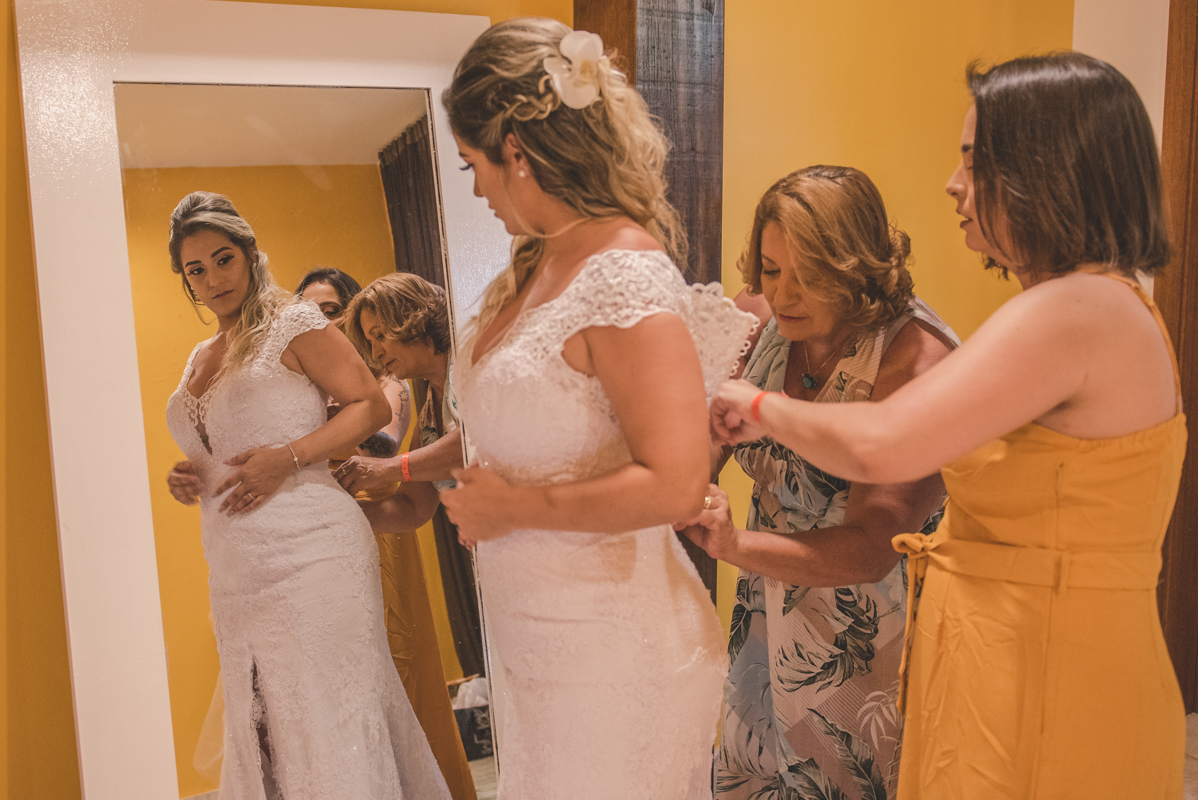 Mãe da noiva fechando vestido junto com sua irmã