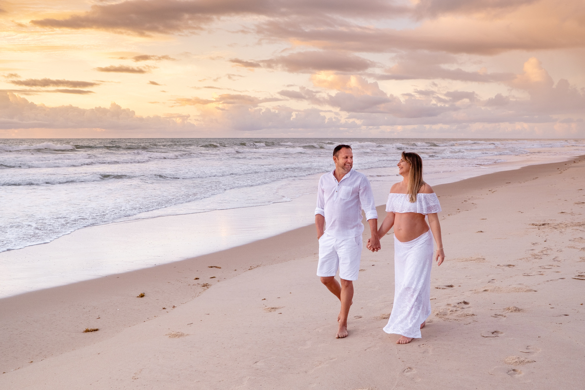 ensaio de gestante na praia, no nascer do sol com marido caminhando na areia