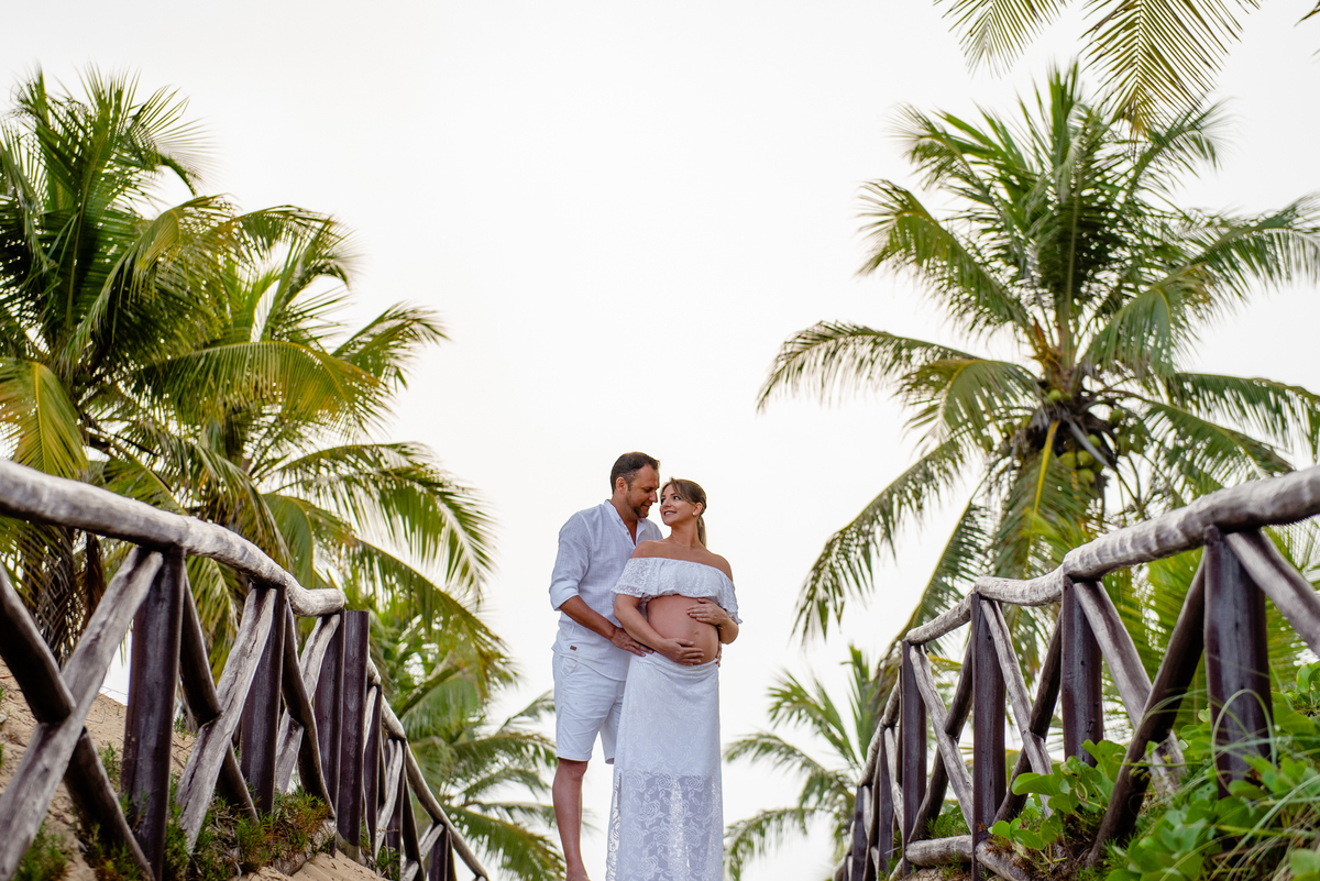 Ensaio de gestante com casal se abraçando perto dos coqueiros na praia e na Bahia