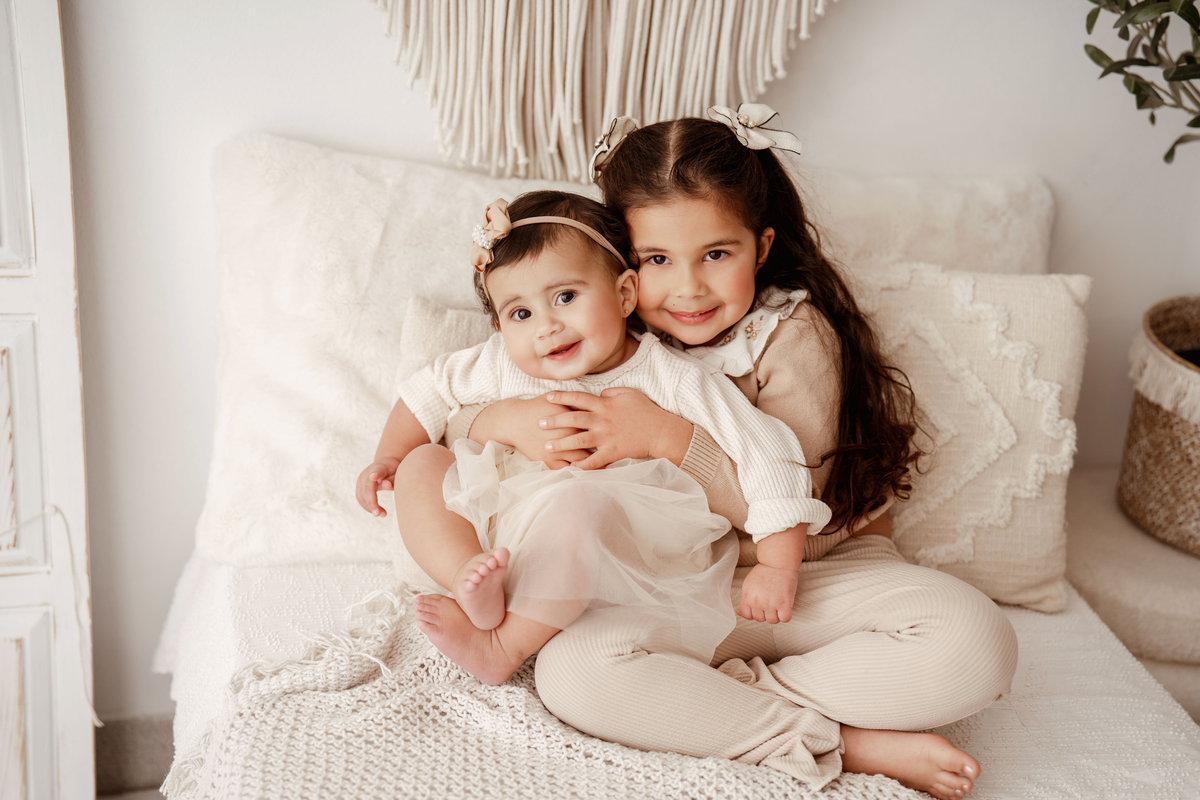 Fotografia de irmãs com bebé de 1 ano em ambiente delicado