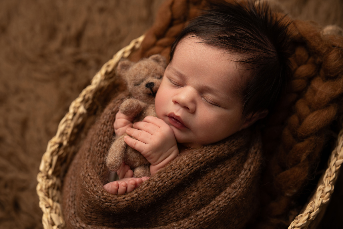 Fotografia newborn de bebé recém-nascido confortavelmente aconchegado num cesto. Sessão realizada em estúdio perto de Lisboa e Oeiras.