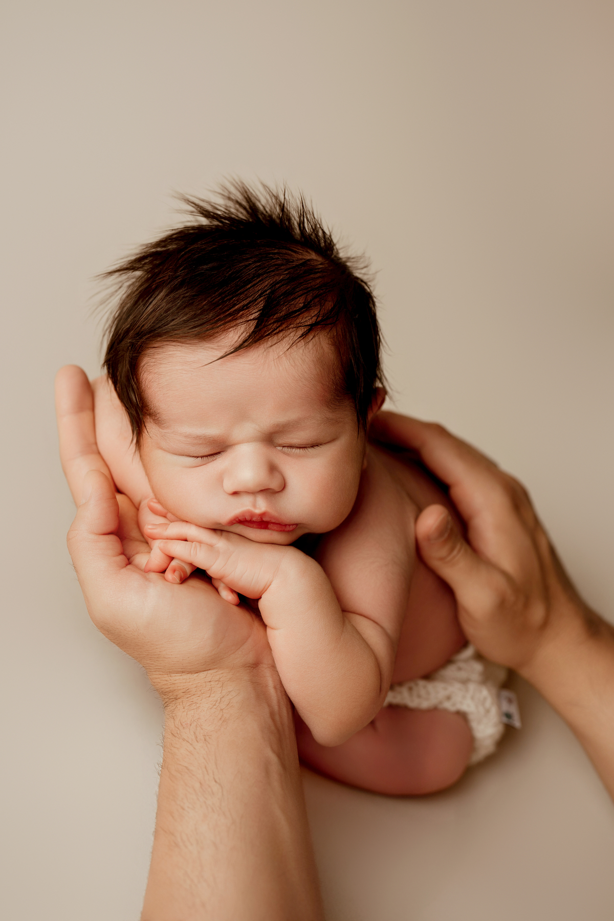 Recém-nascido fotografado com total segurança nas mãos do pai. Imagem captada durante uma sessão newborn em estúdio.