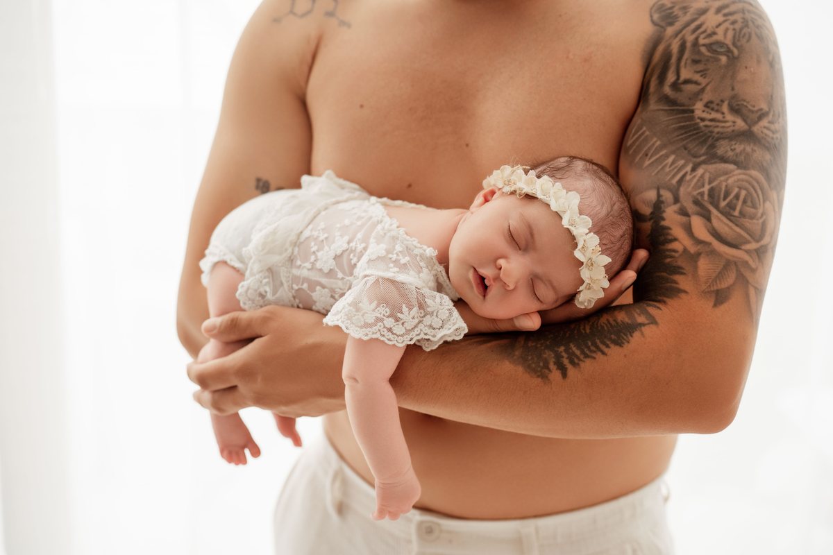 Bebé recém-nascida ao colo do pai durante sessão fotográfica newborn em Oeiras.
