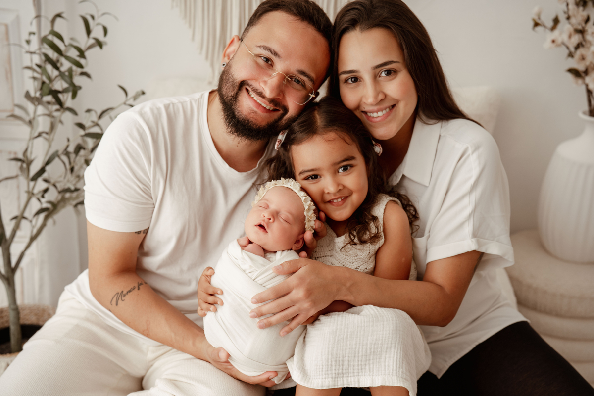 Retrato de família com recém-nascida e irmã mais velha durante sessão newborn em estúdio.
