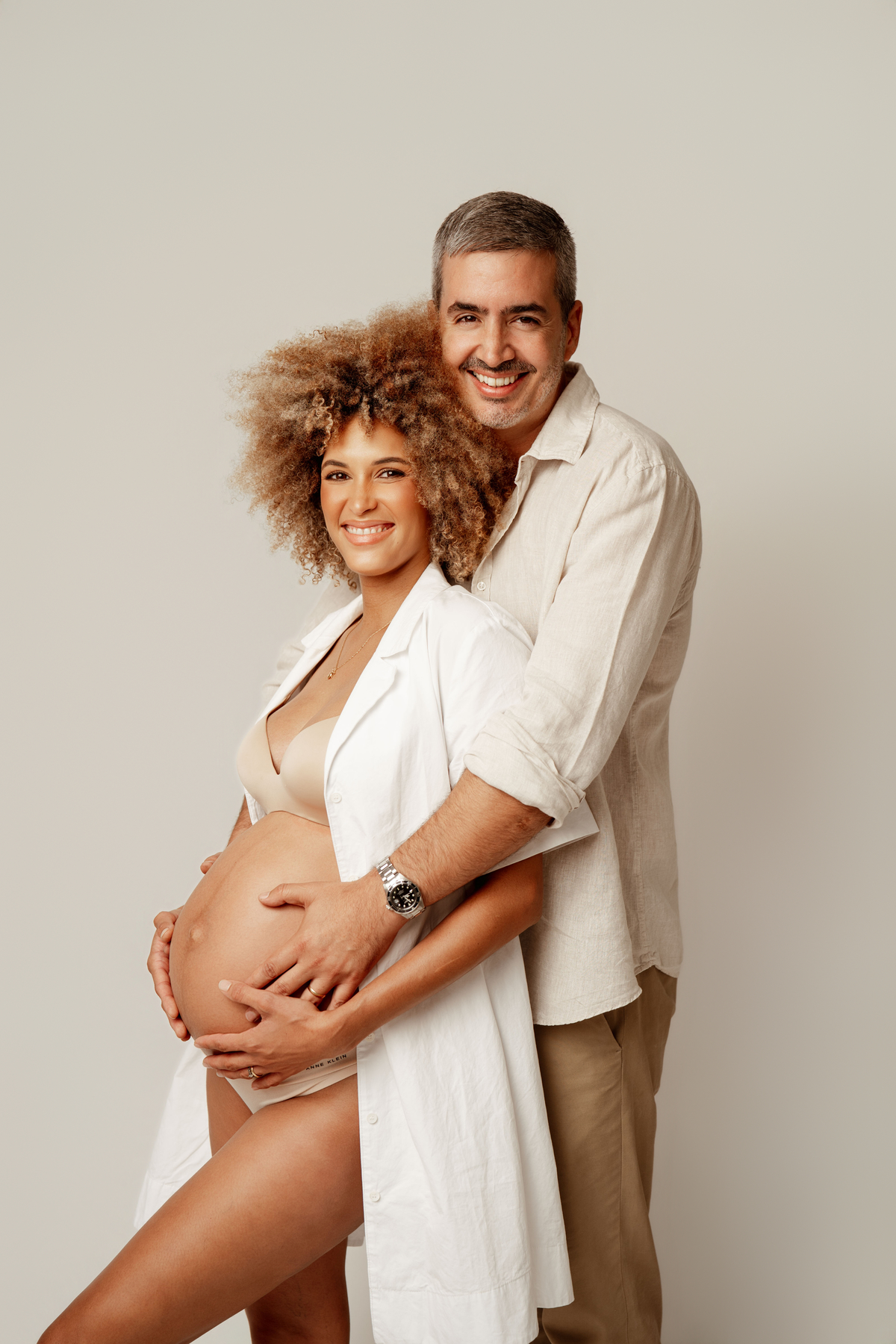 Sessão de gravidez em Lisboa com futuros pais sorridentes e mãos sobre a barriga da grávida.