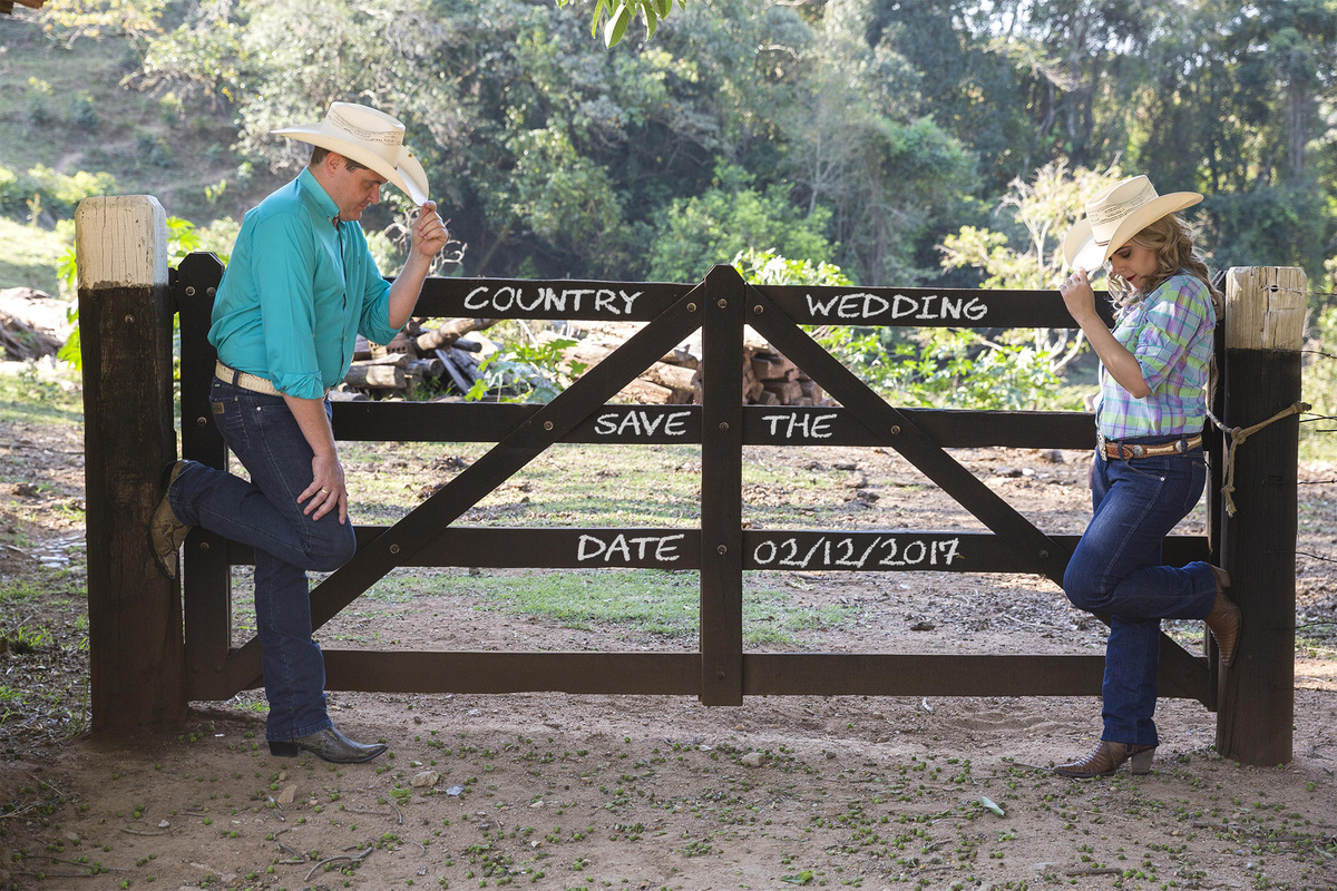 casal de noivos ao lado de cerca em fazenda com escritas save the date wedding country